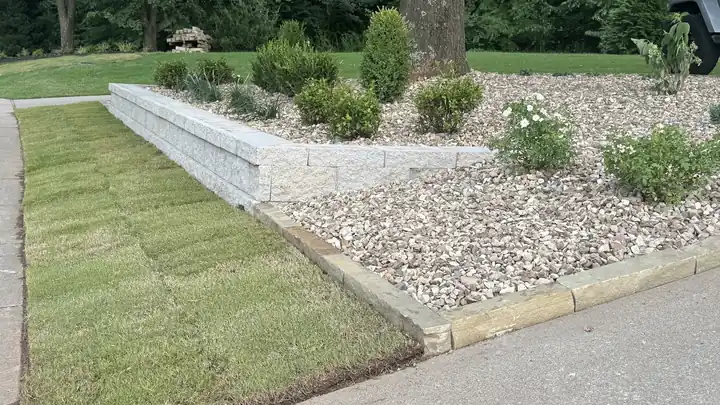 New sod laid along a fresh stacked-block retaining wall and river-rock bed