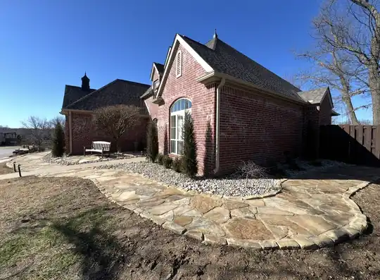 Finished flagstone walkway and patio with a gravel border around the corner of a brick house