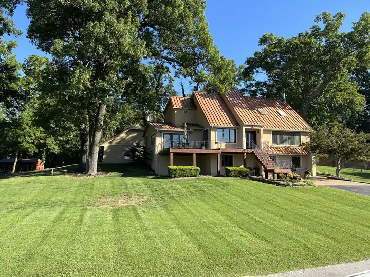 A freshly striped front lawn rising to a two-story home under mature oaks, mowed by Pureleaf